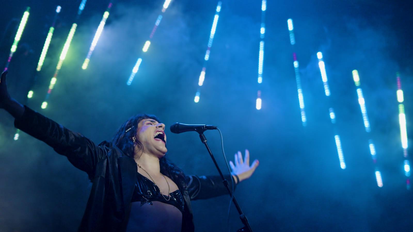 A performer singing with arms outstretched on stage