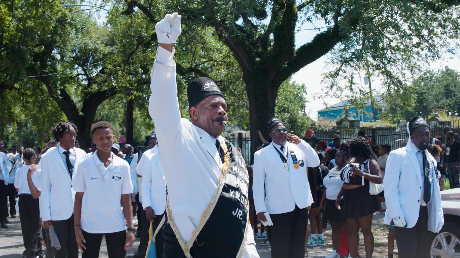 A grand marshal raising his fist at the head of a New Orleans second line