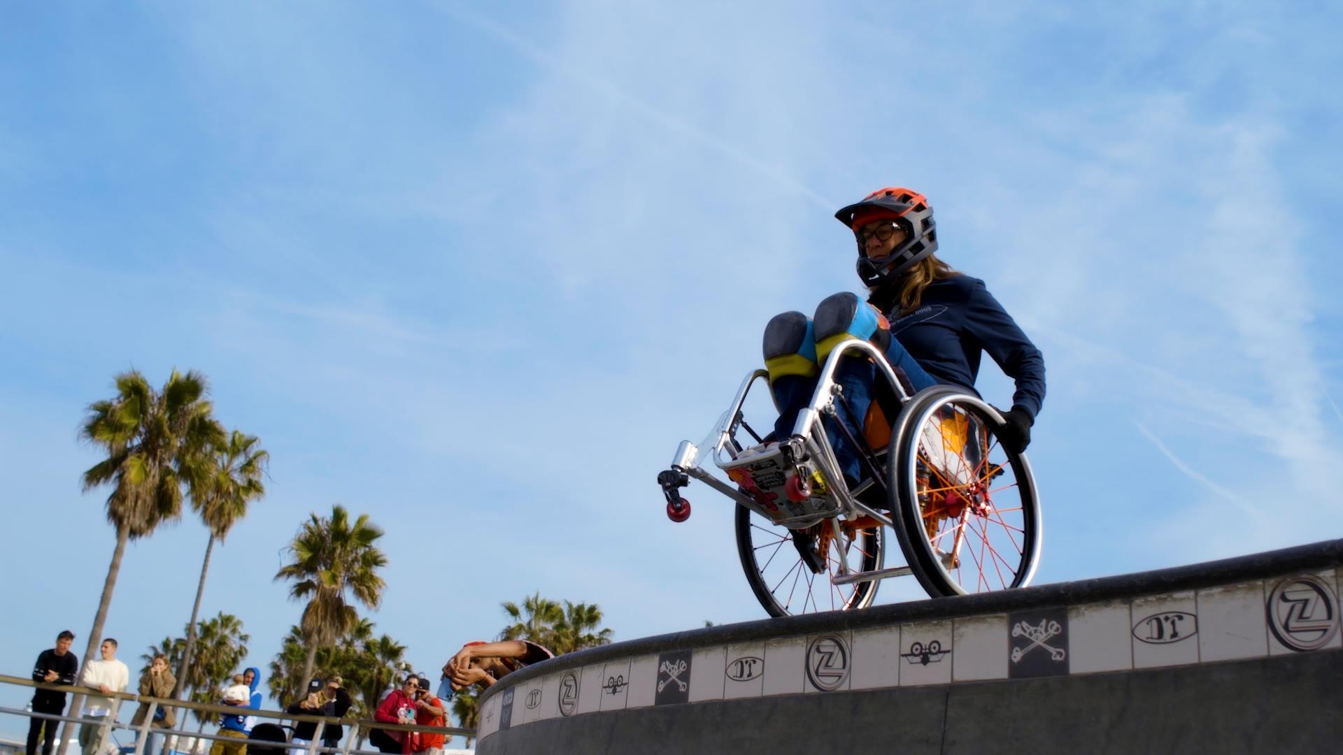 An adaptive athlete dropping into the Venice skate bowl as onlookers watch